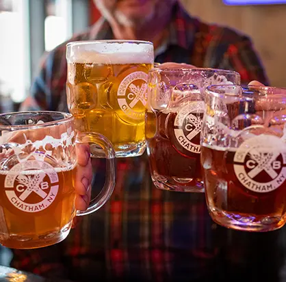 A photo of patrons toasting with mugs of beer at Chatham Brewing.